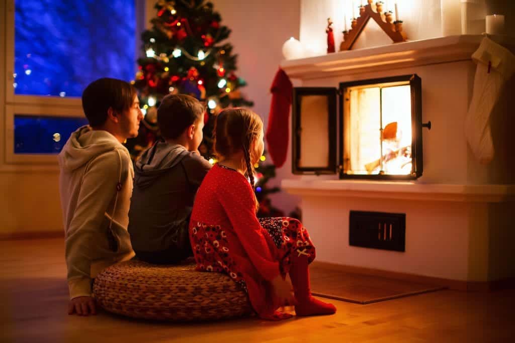 Father and his two little kids sitting by a fireplace in their f